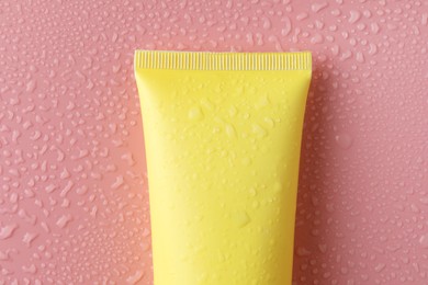 Moisturizing cream in tube on pink background with water drops, top view