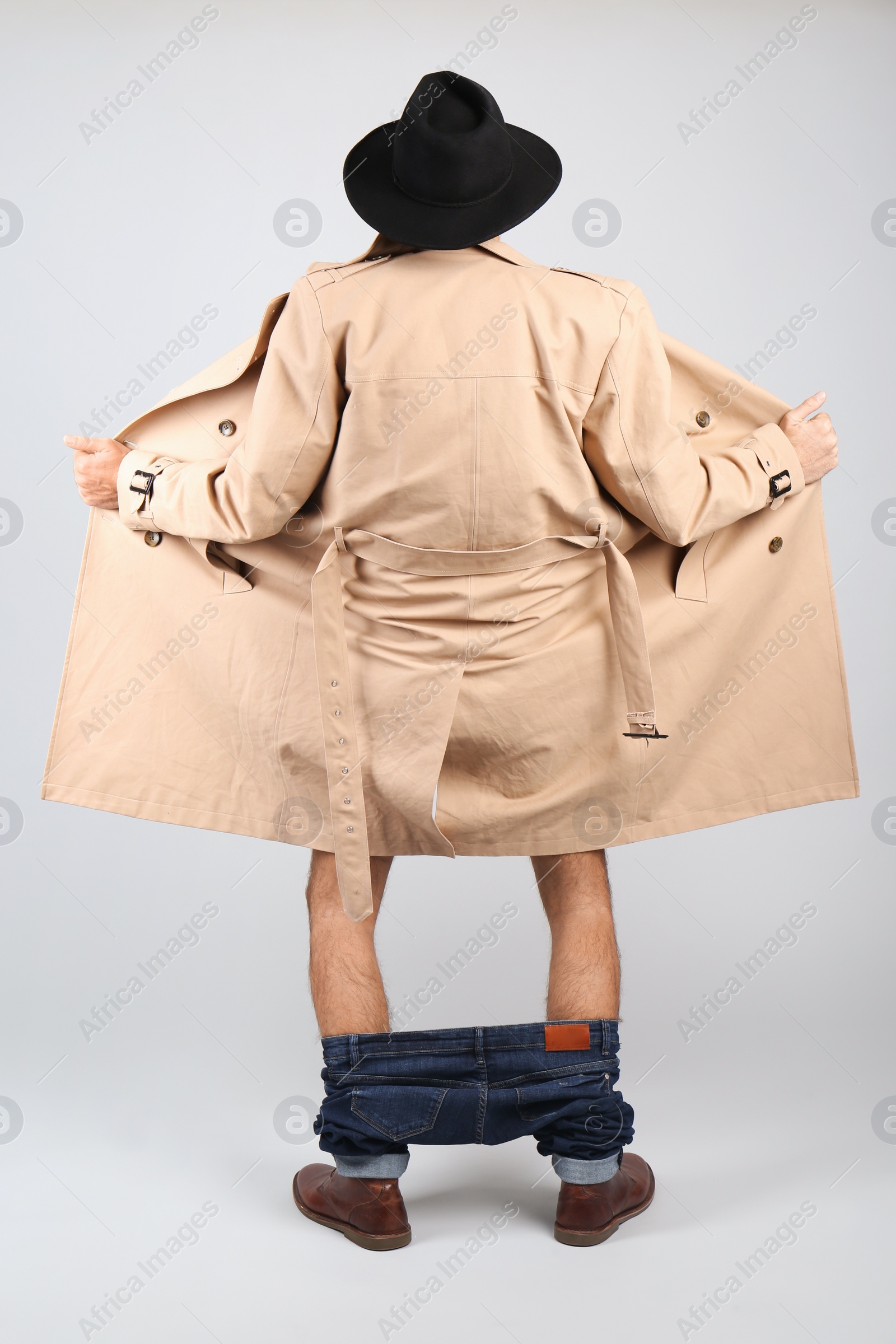 Photo of Exhibitionist exposing naked body under coat on light background, back view