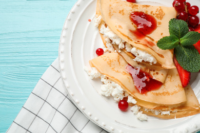 Delicious thin pancakes with cottage cheese, jam and berries on light blue wooden table, flat lay