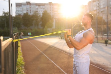Photo of Muscular man doing exercise with elastic resistance band outdoors at sunset