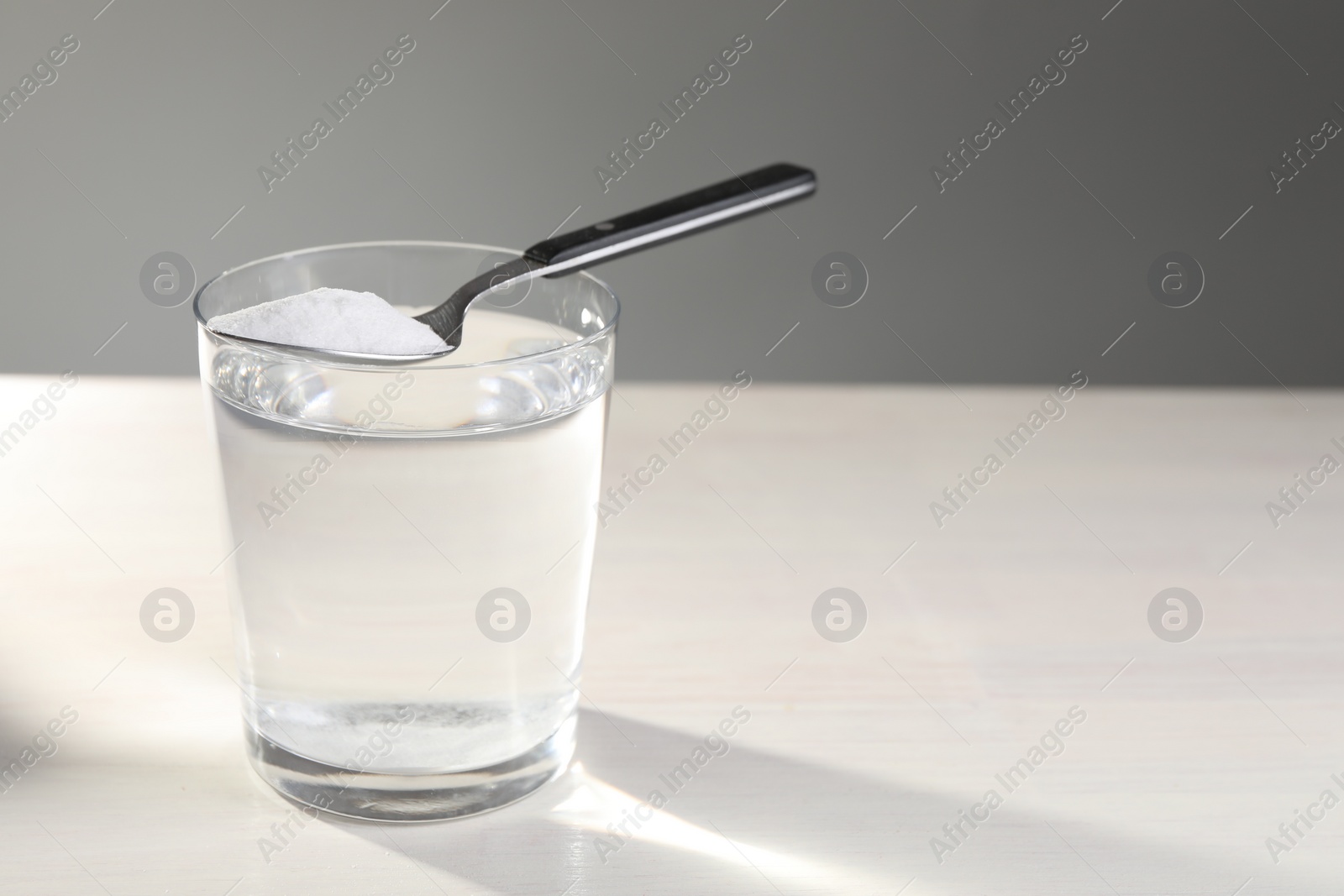 Photo of Glass of water and spoon with baking soda on white table. Space for text