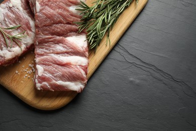 Photo of Raw ribs with rosemary and salt on black table, top view