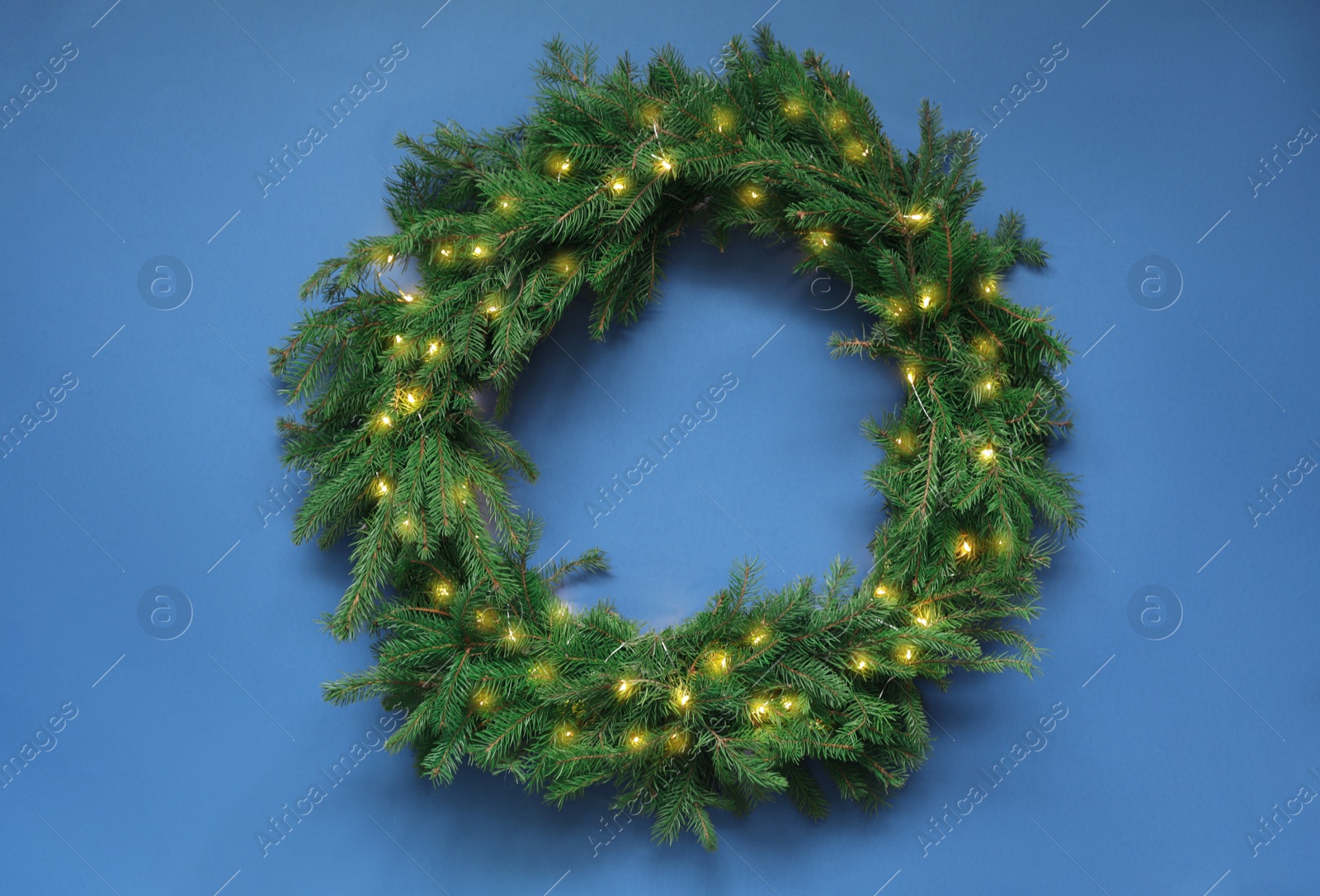 Photo of Beautiful Christmas wreath with festive lights on blue background, top view