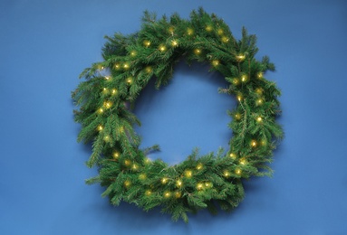 Photo of Beautiful Christmas wreath with festive lights on blue background, top view