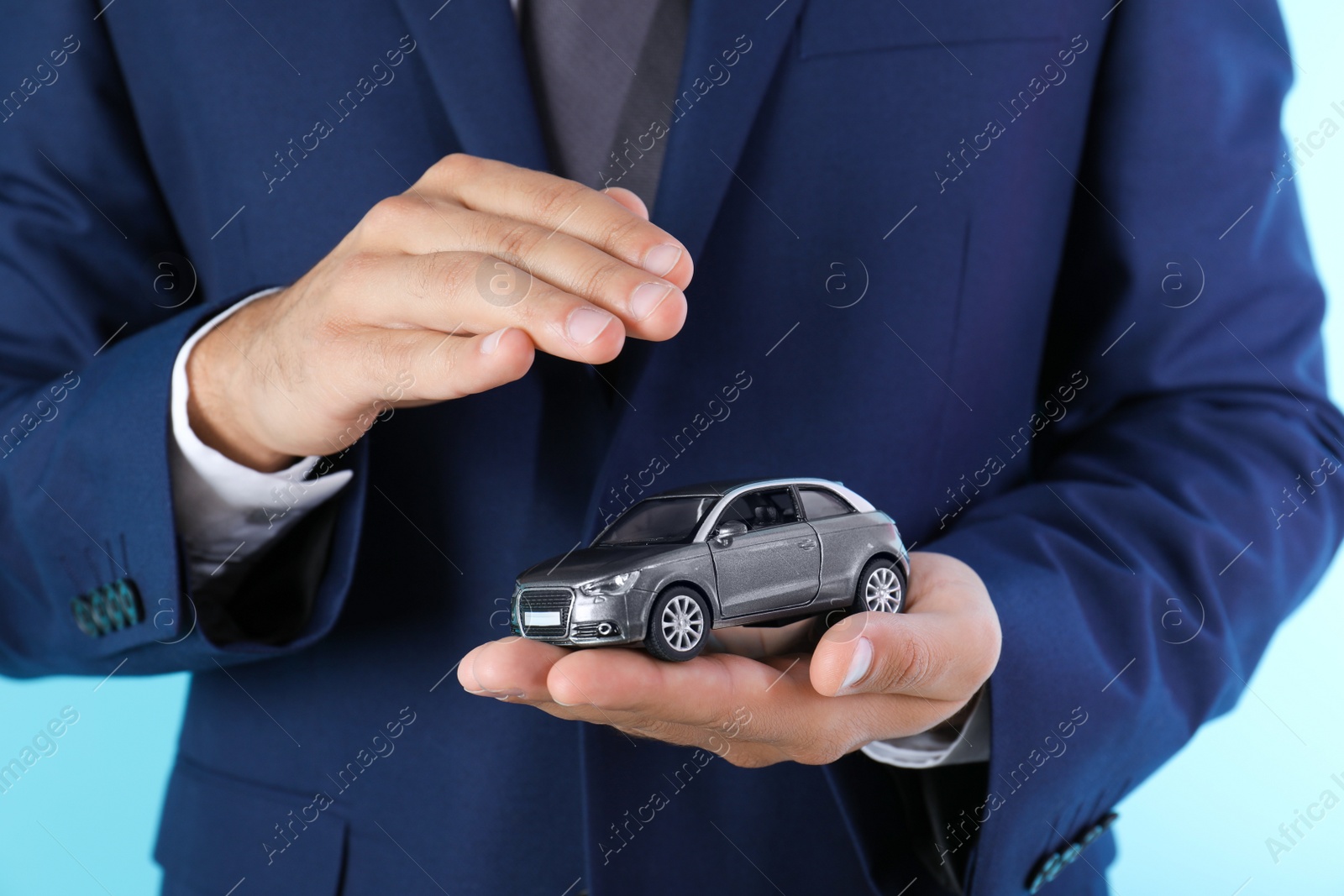 Photo of Insurance agent holding toy car on color background, closeup