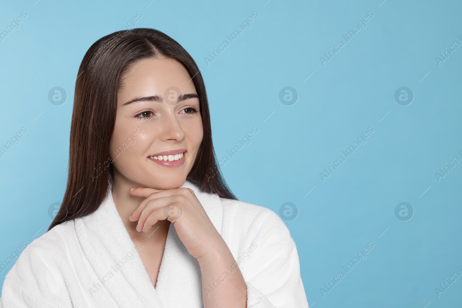 Photo of Portrait of attractive young woman in bathrobe on light blue background, space for text. Spa treatment