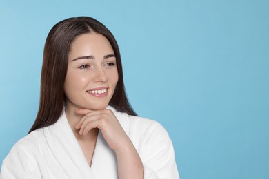 Photo of Portrait of attractive young woman in bathrobe on light blue background, space for text. Spa treatment