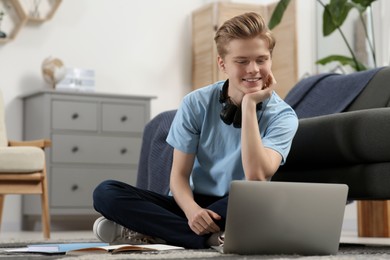 Photo of Online learning. Smiling teenage boy looking on laptop at home