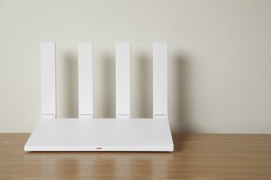 Photo of New modern Wi-Fi router on wooden table near white wall. Space for text