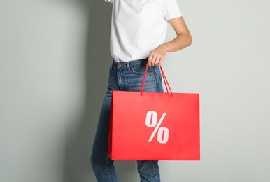 Image of Discount, sale, offer. Woman holding paper bag with percent sign against light background, closeup