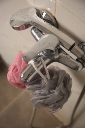 Photo of Colorful shower puffs hanging on faucet in bathroom, above view