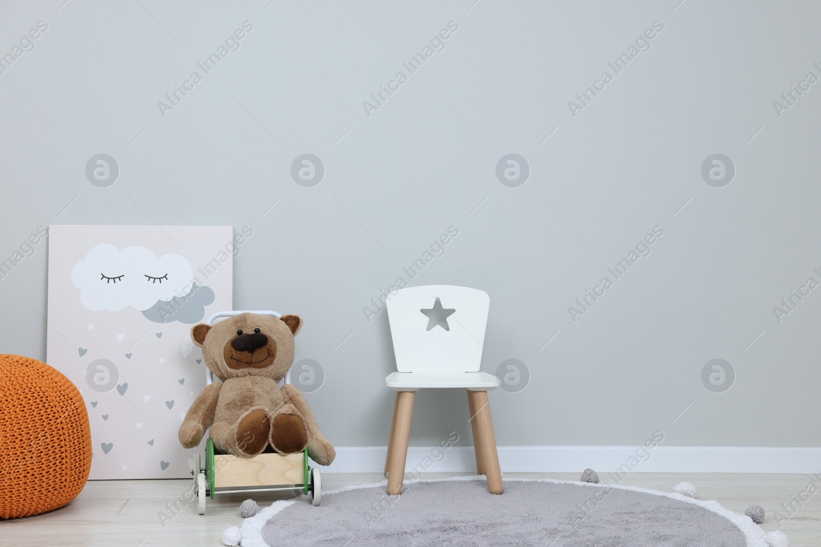 Photo of Kindergarten interior. Small chair, toy, ottoman and picture near grey wall, space for text