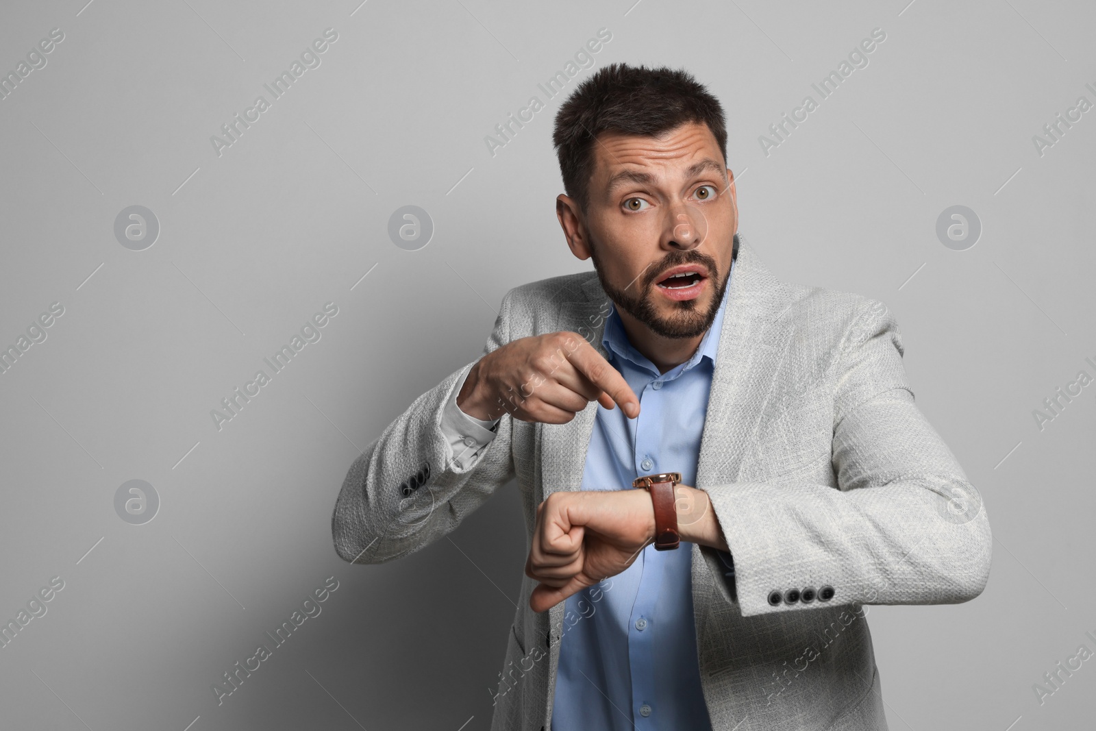 Photo of Emotional man checking time on grey background, space for text. Being late concept