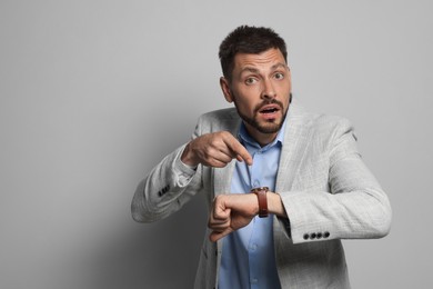 Emotional man checking time on grey background, space for text. Being late concept