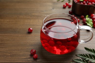 Tasty hot cranberry tea in glass and fresh berries on wooden table