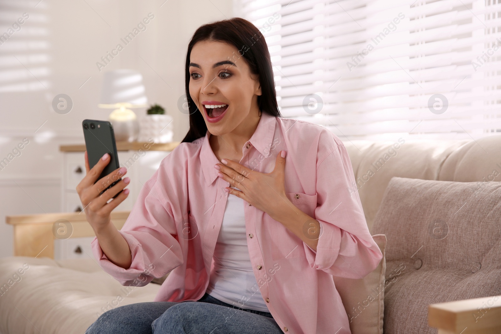 Photo of Emotional woman participating in online auction using smartphone at home