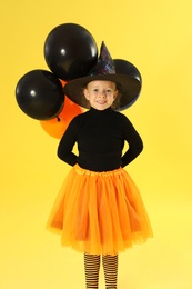 Photo of Cute little girl with balloons wearing Halloween costume on yellow background