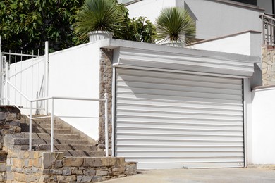 Building with white roller shutter garage door, stairs and gate outdoors
