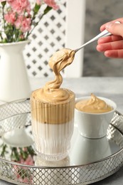 Photo of Woman pouring cream for dalgona coffee into glass at table, closeup