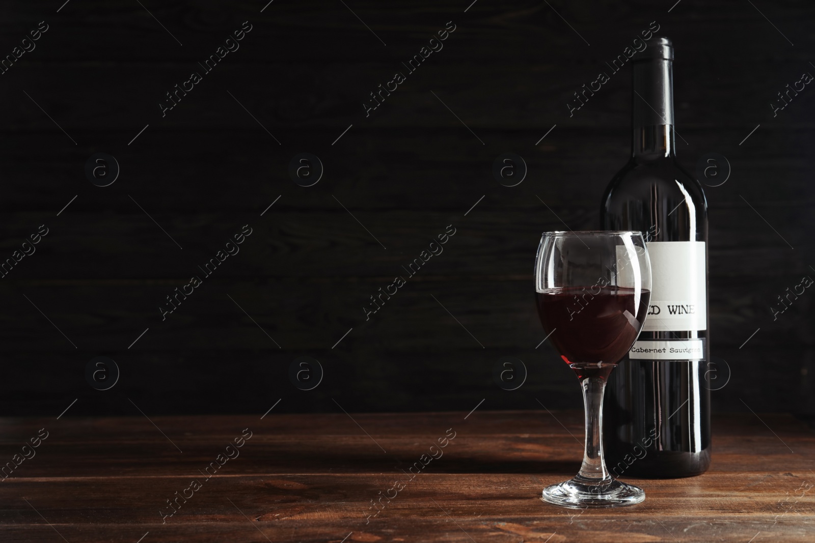 Photo of Glass and bottle with delicious red wine on table against dark background
