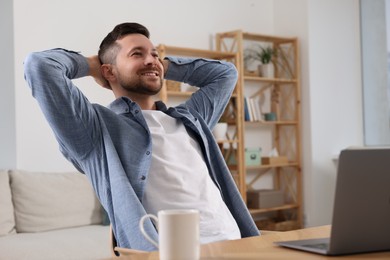 Photo of Happy man having break while working with laptop at wooden desk in room