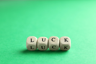 Word LUCK made with wooden cubes on green background, closeup