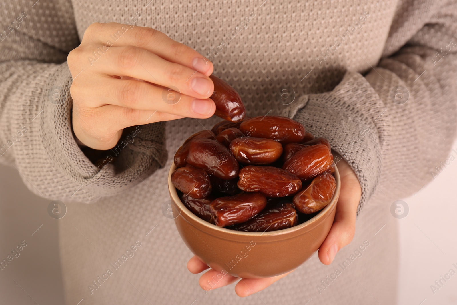 Photo of Woman with bowl of tasty sweet dried dates on light background, closeup