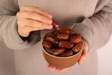 Woman with bowl of tasty sweet dried dates on light background, closeup