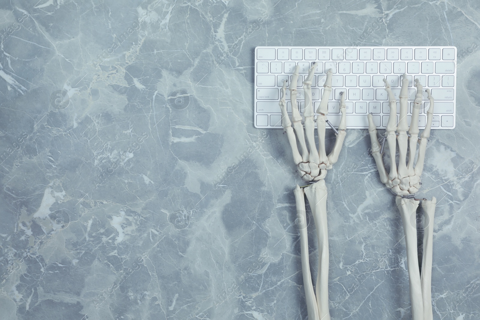 Photo of Human skeleton using computer keyboard at grey marble table, top view. Space for text