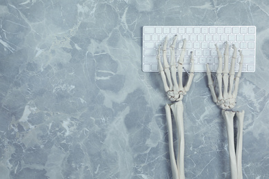 Photo of Human skeleton using computer keyboard at grey marble table, top view. Space for text