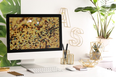 Modern workplace with computer and golden decor on desk near wall. Stylish interior design