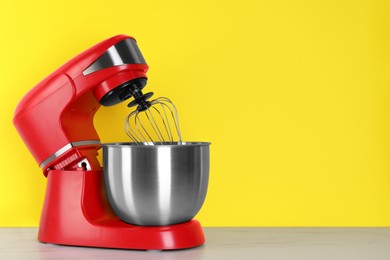 Photo of Modern red stand mixer on white wooden table against yellow background, space for text