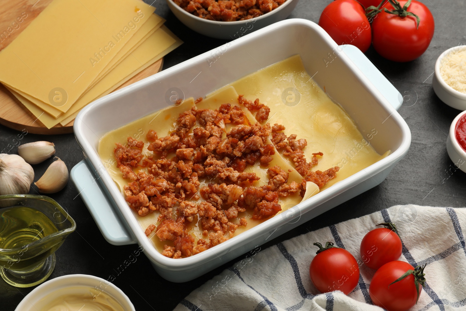 Photo of Cooking lasagna. Pasta sheets, minced meat in baking tray and products on dark table