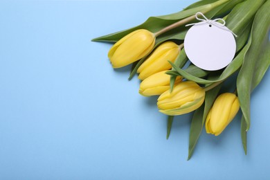 Photo of Bouquet of beautiful yellow tulips and blank card on light blue background, top view with space for text. Birthday celebration