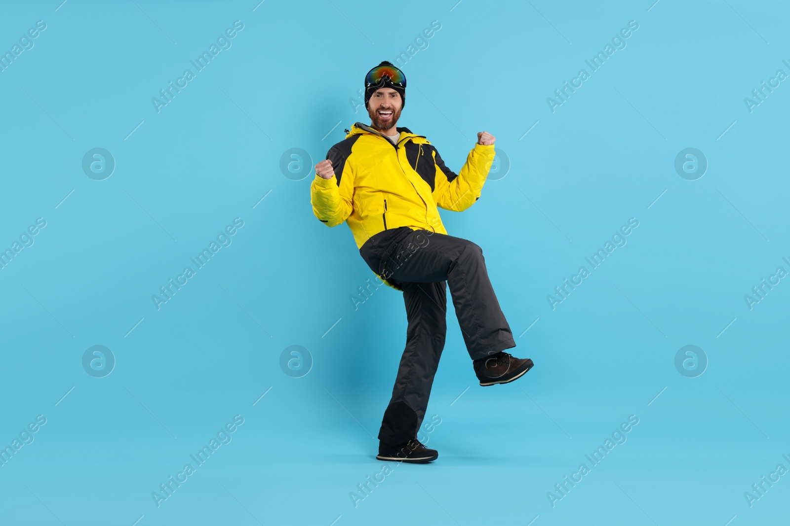 Photo of Winter sports. Cheerful man in ski suit and goggles on light blue background