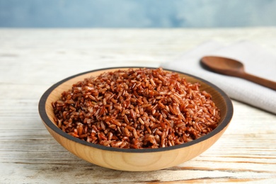 Photo of Bowl with delicious cooked brown rice on white wooden table