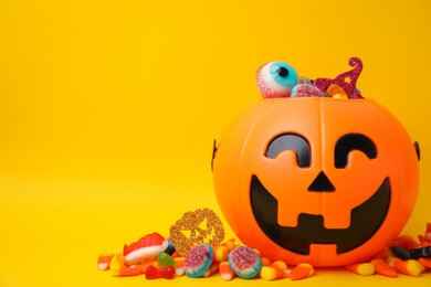 Photo of Halloween trick or treat bucket with different sweets on yellow background, space for text