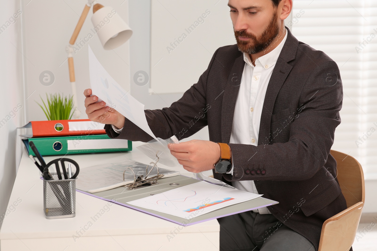 Photo of Businessman putting document into punched pocket at white table in office