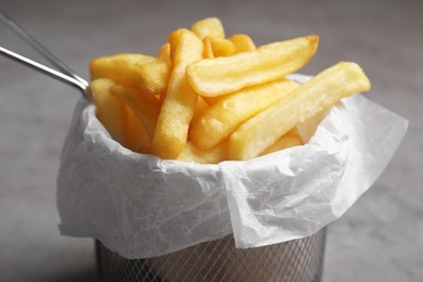 Photo of Frying basket with tasty french fries on light grey background, closeup