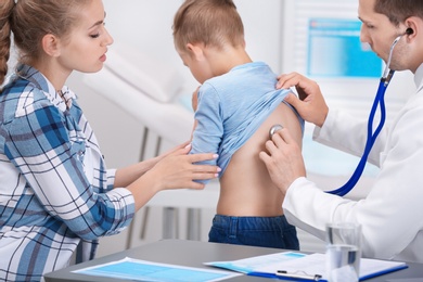 Doctor examining coughing little boy at clinic