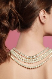 Young woman wearing elegant pearl necklace on pink background, back view
