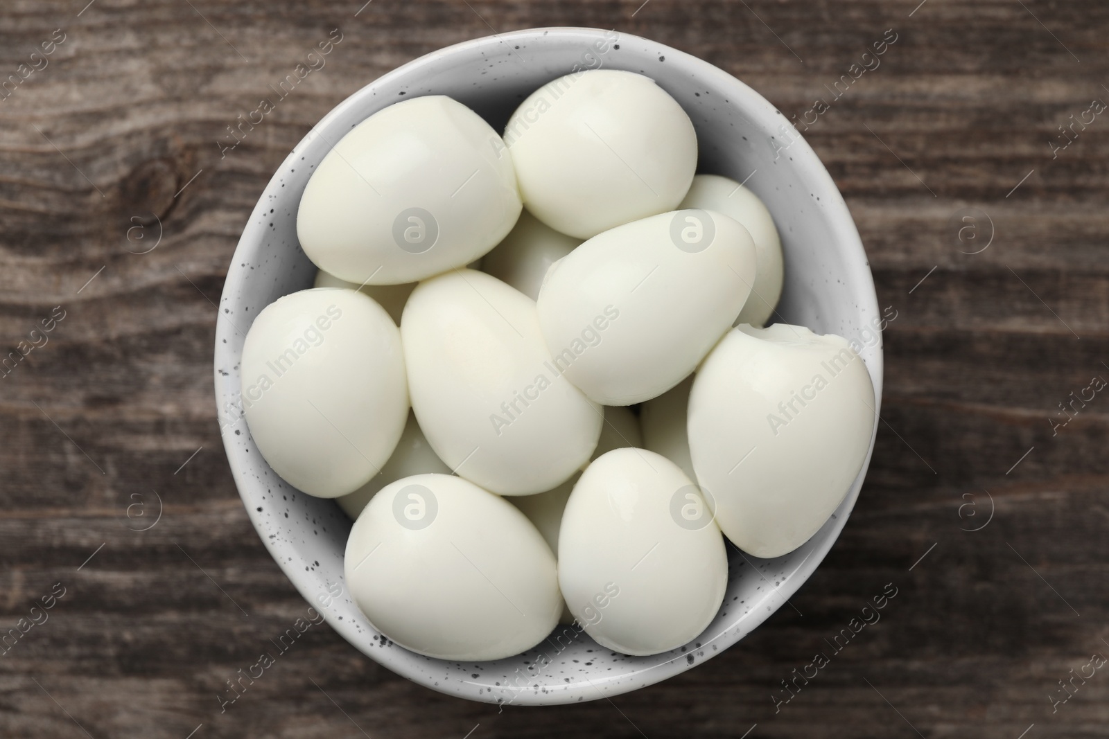 Photo of Many peeled boiled quail eggs in bowl on wooden table, top view