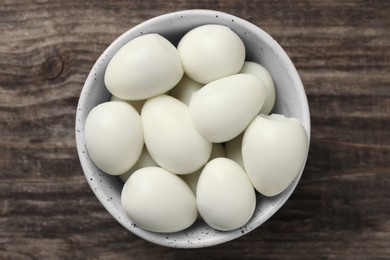 Many peeled boiled quail eggs in bowl on wooden table, top view