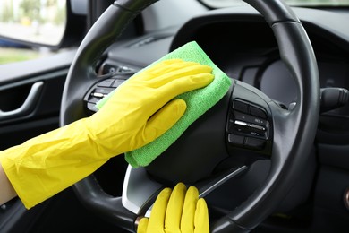 Photo of Woman cleaning steering wheel with rag in car, closeup