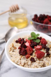 Photo of Oatmeal with freeze dried strawberries and mint on white marble table