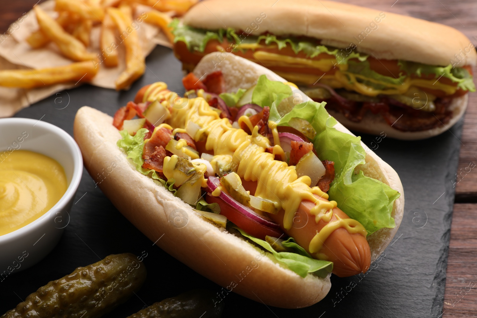 Photo of Delicious hot dogs with lettuce, onion and pickle served on table, closeup