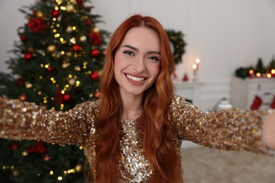 Happy young woman taking selfie in room decorated for Christmas