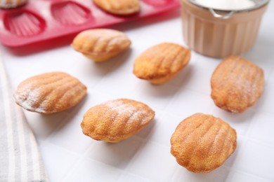 Photo of Delicious madeleine cookies and baking mold on white tiled table, closeup