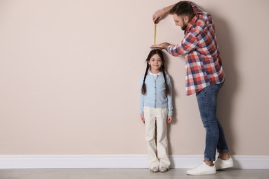 Photo of Father measuring daughter's height near beige wall indoors, space for text