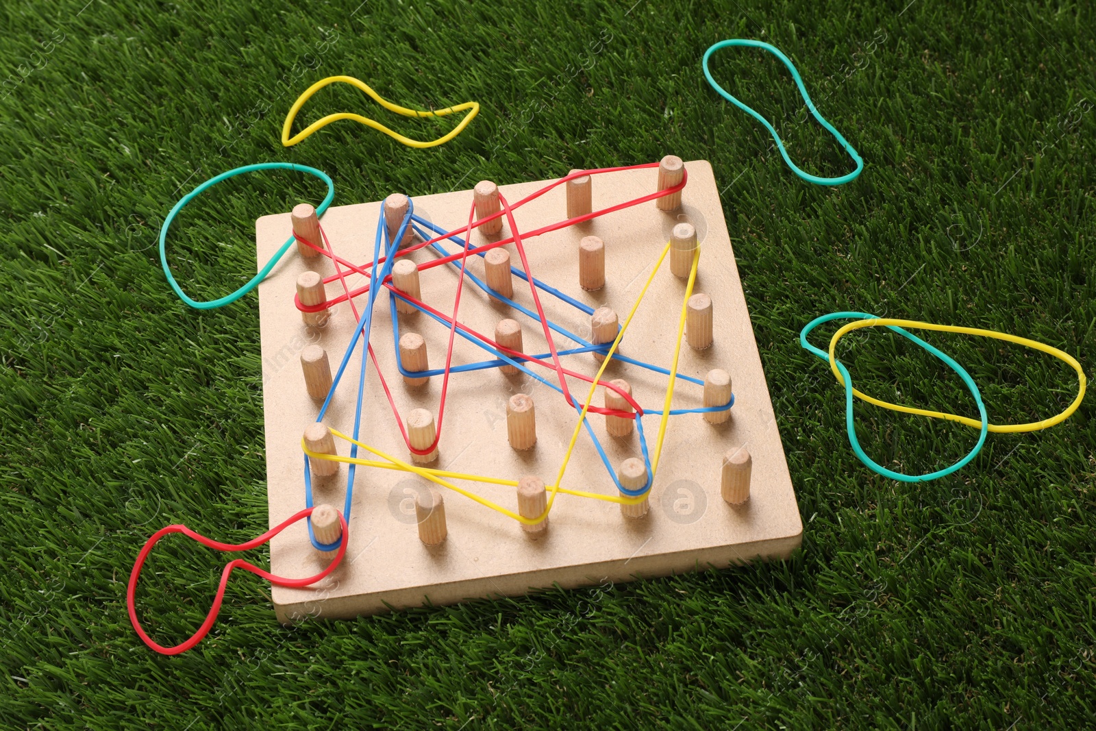 Photo of Wooden geoboard with rubber bands on artificial grass. Educational toy for motor skills development